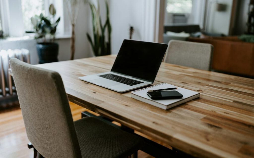 A wooden desk with a laptop, notebook and coffee mug