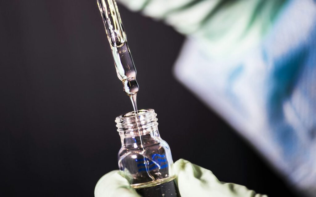 A pipette dropping liquid into a small vial in a lab
