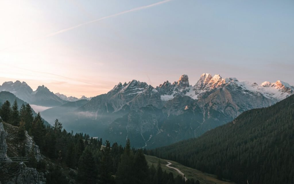 A mountain valley at dawn with forested slopes and snowy peaks