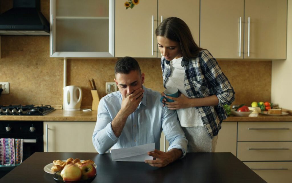 A woman sitting at a table looking worried over a pile of bills