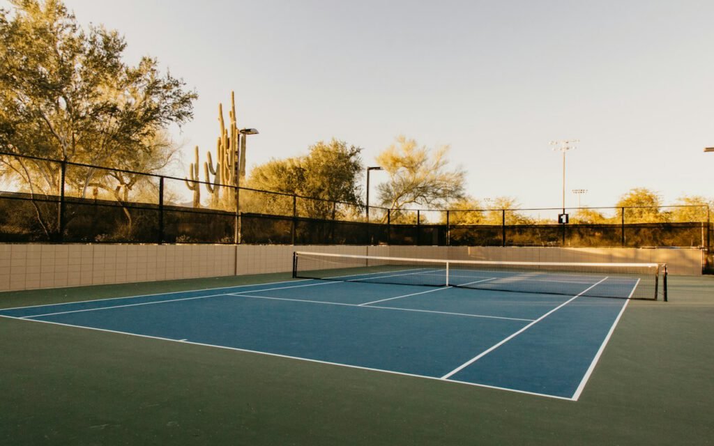 An empty hard tennis court with a net in the afternoon light
