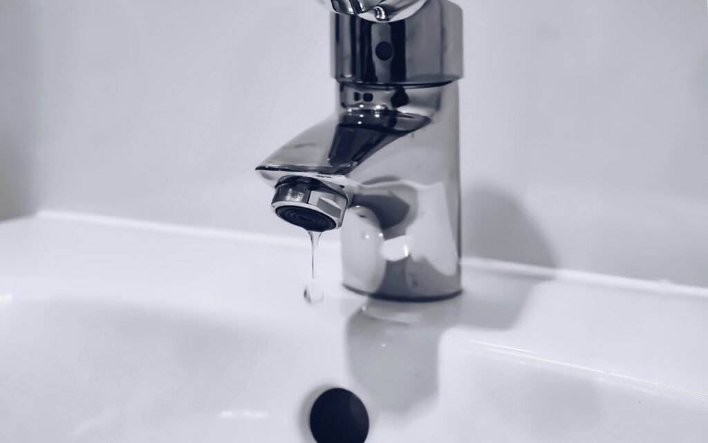 A faucet with a slow drip of water falling into a sink