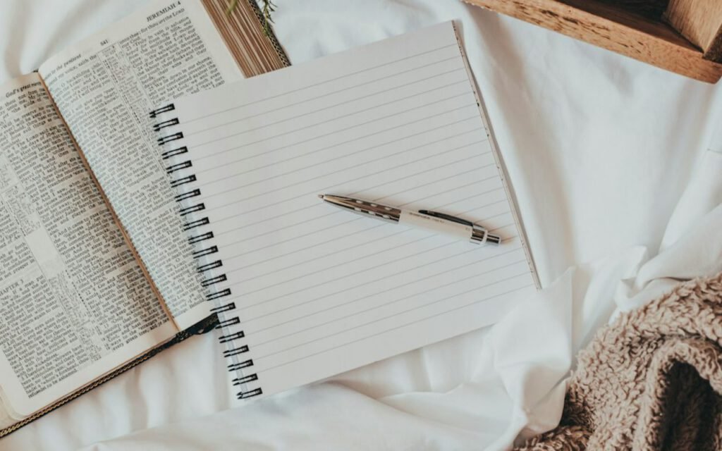 A notebook and pen beside a cup of coffee on a wooden table
