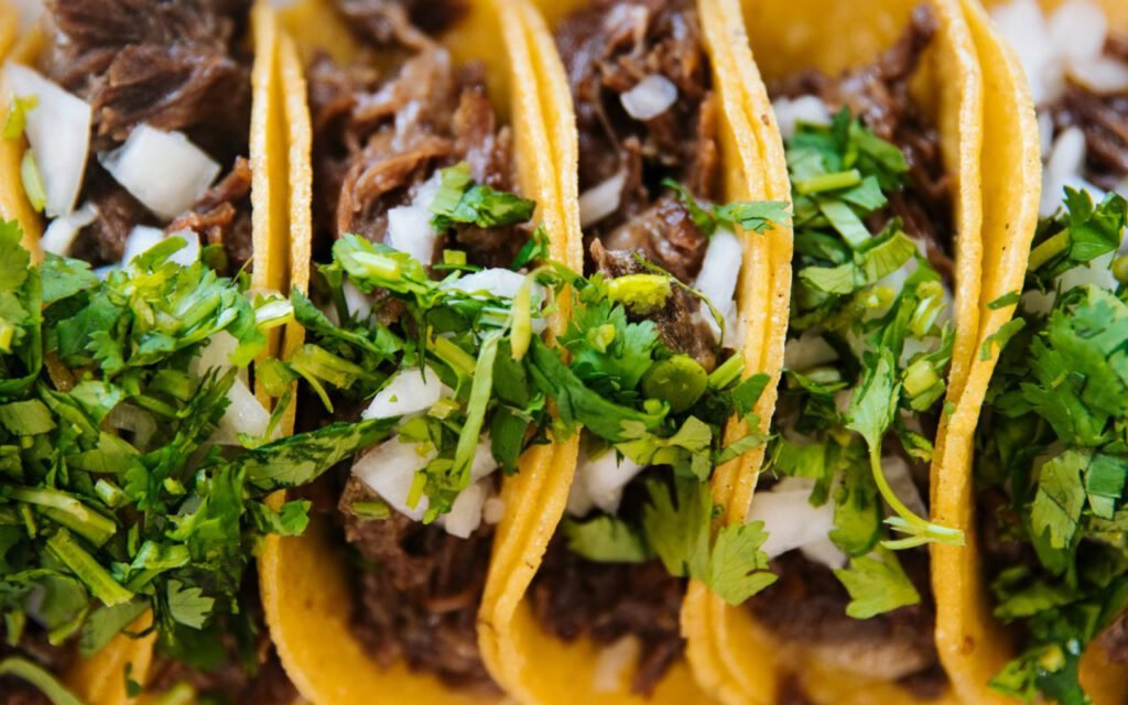A row of tacos topped with fresh garnishes