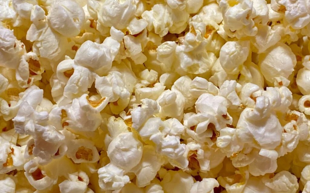A striped bucket of popcorn held in front of a movie screen