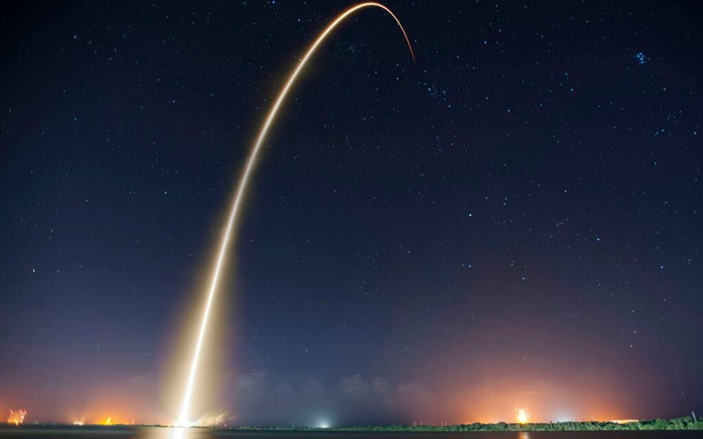 A curving rocket exhaust trail glowing in the early morning sky