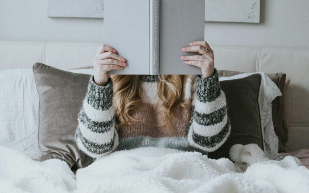 Person reading a paperback in bed under a warm blanket