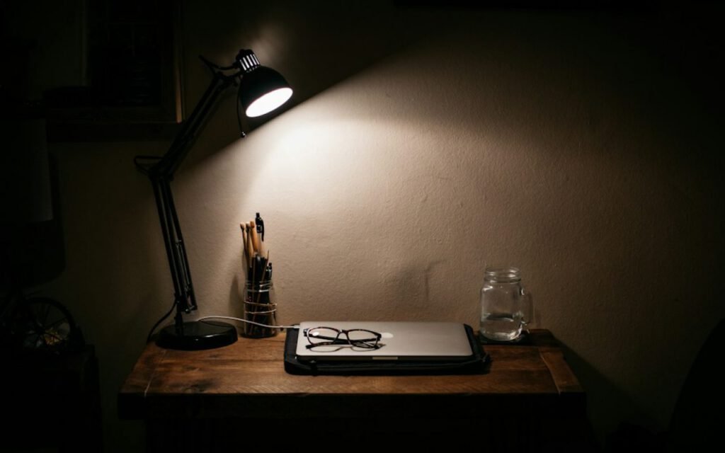 A warm desk lamp glowing over a wooden writing desk