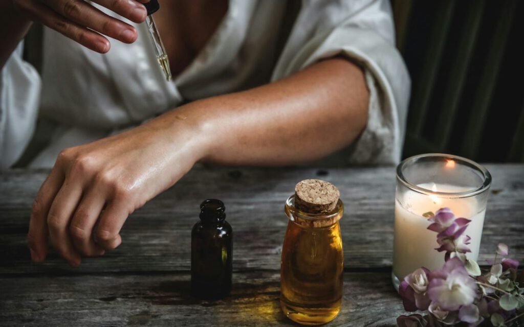 A lit candle beside small bottles of oil on a bathroom shelf
